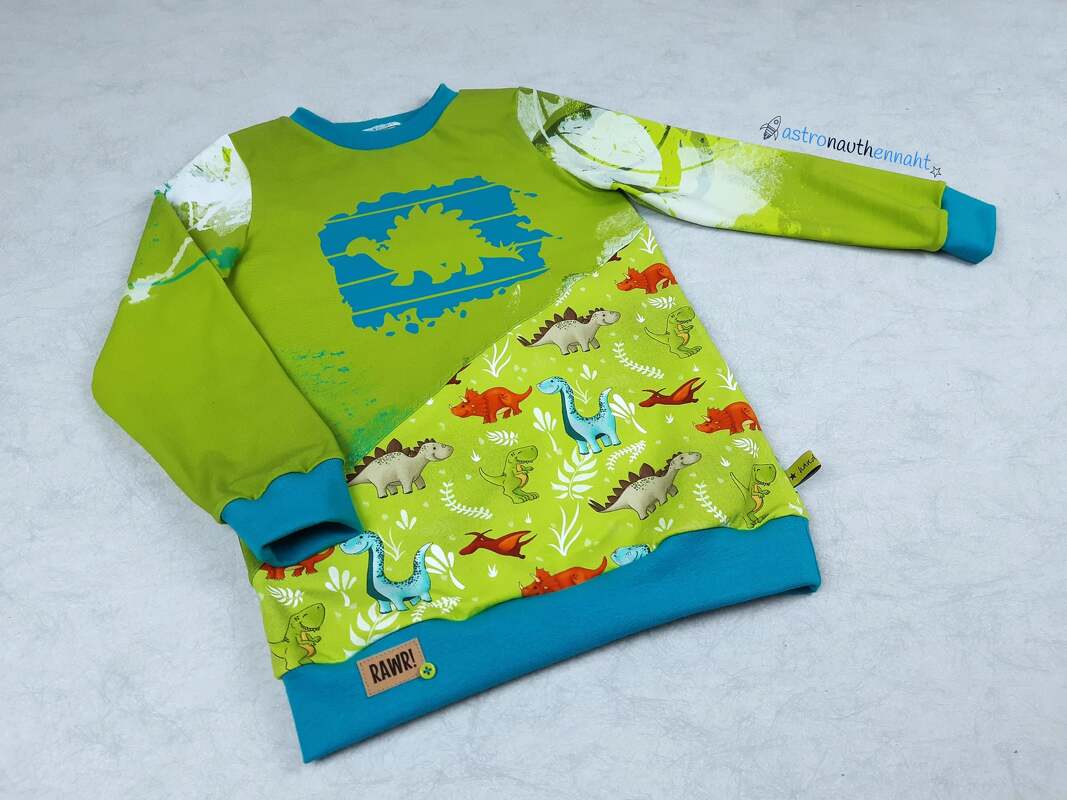 Grüner Kinderpullover mit blauem Dinosaurier-Plott und gemustertem Dino-Stoff