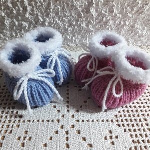 Zwei handgestrickte Babyschuhe in Hellblau und Rosa mit weißem Plüschrand