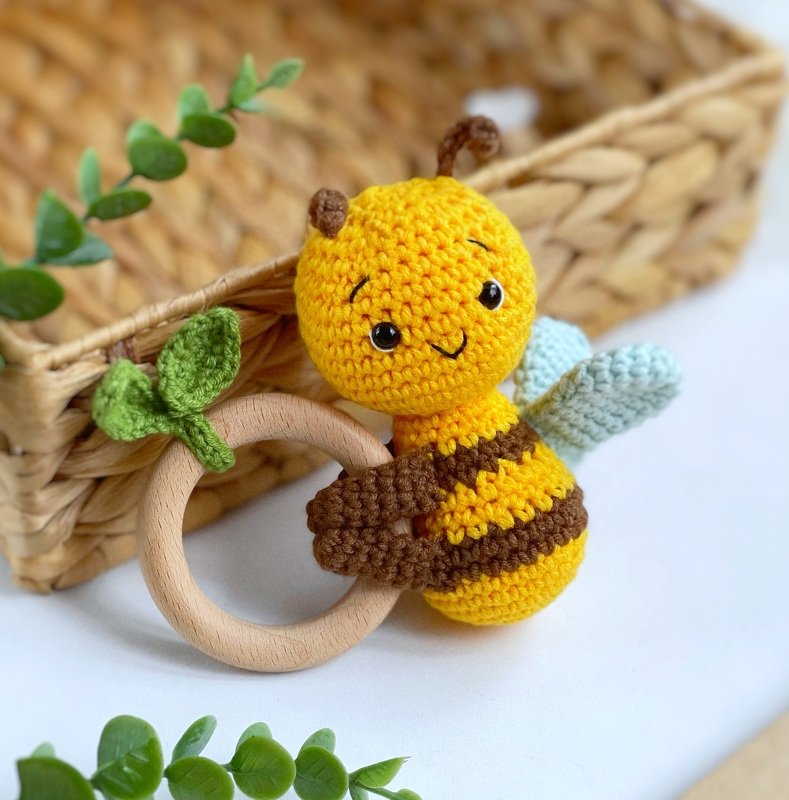 Yellow and brown crocheted bee attached to a wooden ring with a green crochet leaf and pale blue wings