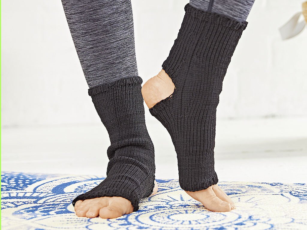 Schwarze gestrickte Fußwärmer mit offener Ferse und freiem Vorfuß auf gemusterter Matte