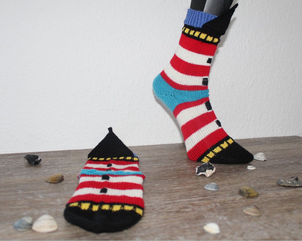 Gestrickte Socken mit rot-weißen Streifen, blauer Ferse, schwarzer Spitze und gelben Fenster-Details; ein Socken flach, einer auf Fußmodell