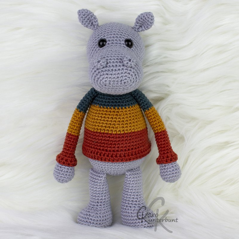 Gehäkeltes Nilpferd-Amigurumi mit gestreiftem Pullover auf hellem Fell