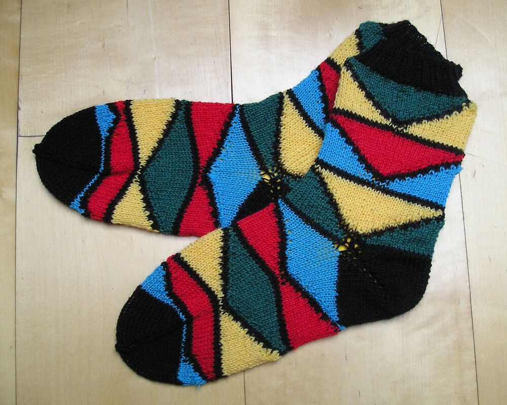 Paar gestrickter Damensocken mit diagonalen Rauten in Schwarz, Rot, Blau, Gelb und Grün auf hellem Holzuntergrund