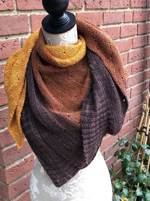 Gestricktes Dreieckstuch mit Farbverlauf in Gelb, Orange und Dunkelbraun auf einer Schneiderpuppe vor einer Ziegelwand.