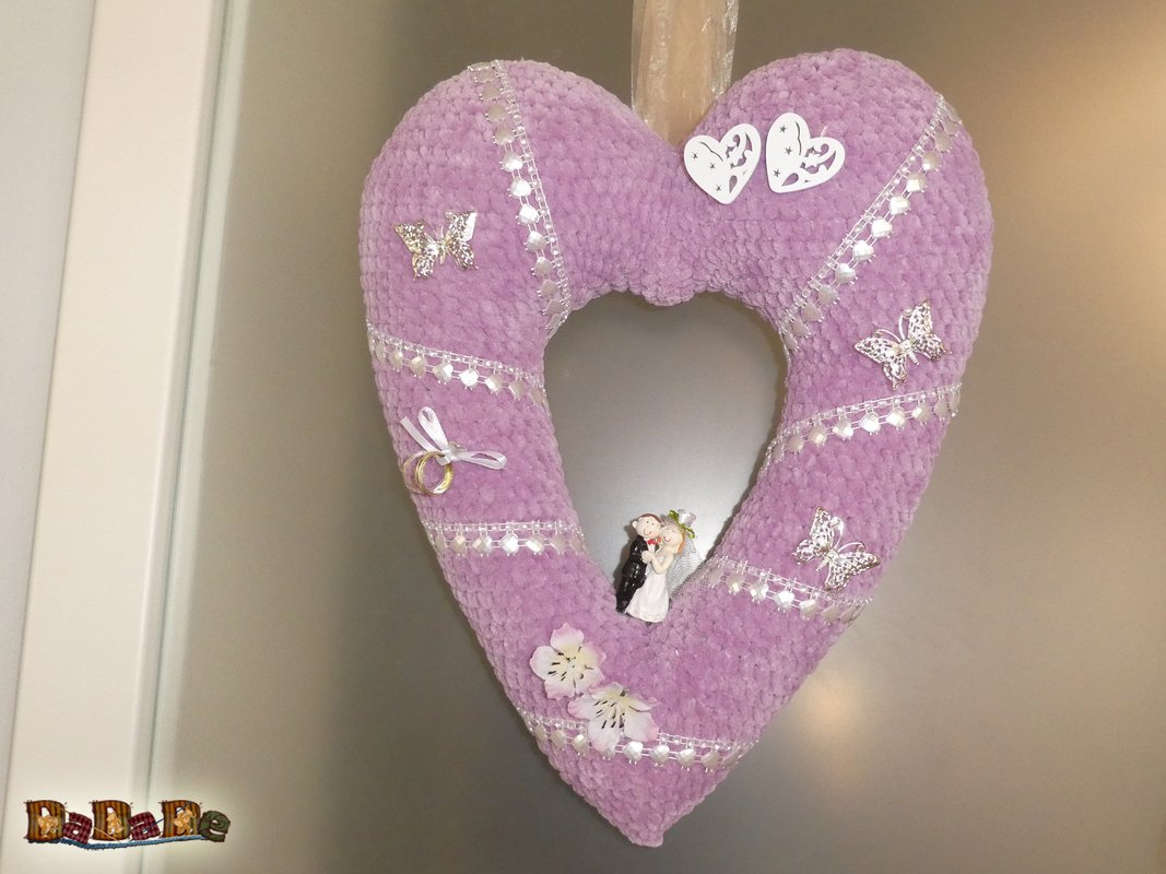 Gehäkelter Herzkranz in Flieder mit silbernen Bändern, Schmetterlings- und Blumenapplikationen sowie Brautpaar‑Figur