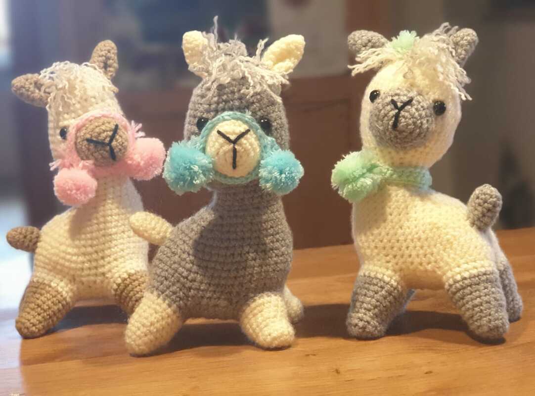 Drei gehäkelte Alpaka-Amigurumi in Pastellfarben mit Pompons