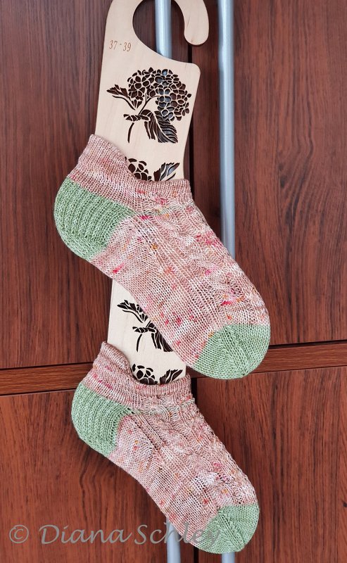 Knitted ankle socks with speckled pink and peach body and mint-green heels and toes on a floral wooden sock blocker marked 37-39.