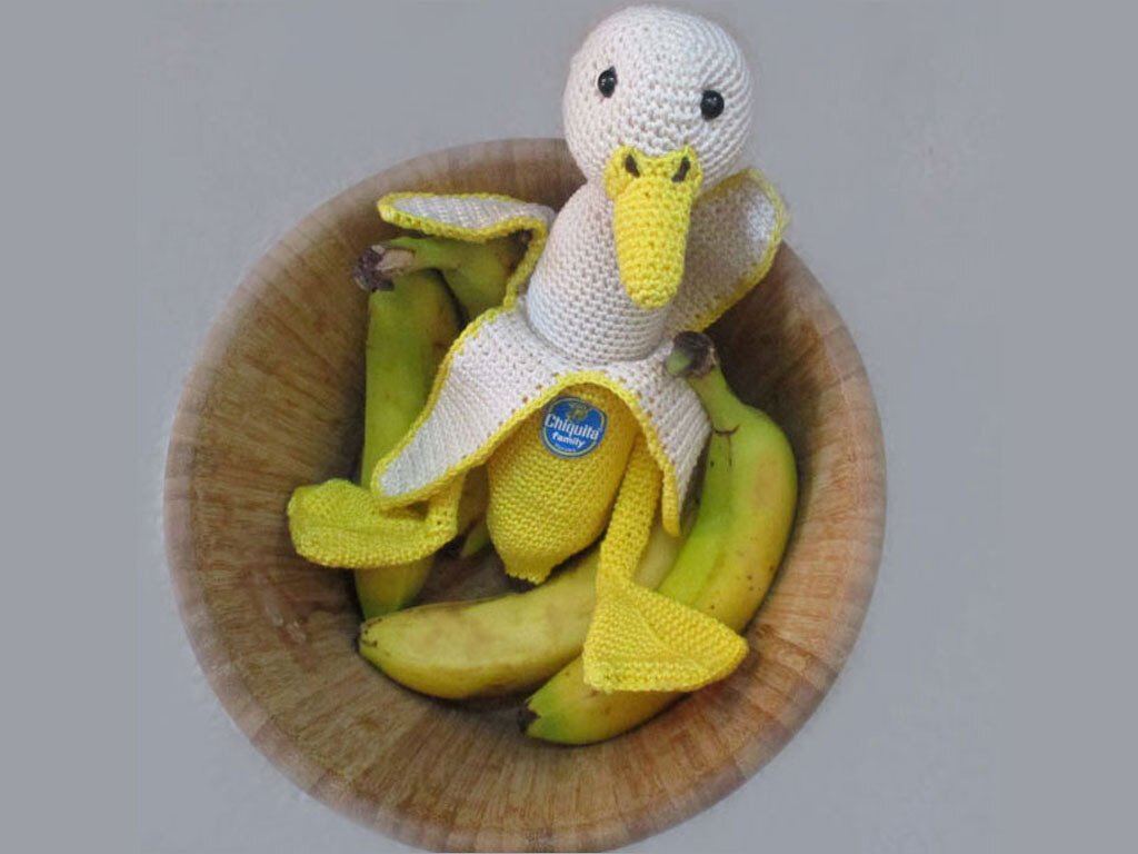 Handgehäkelte Ente in Bananenschale zwischen Bananen in einer Holzschale