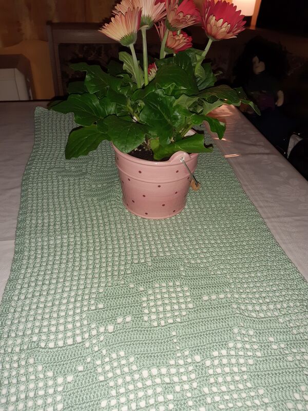 Hellgrüner gehäkelter Tischläufer mit rosa Blumentopf auf weißer Tischdecke