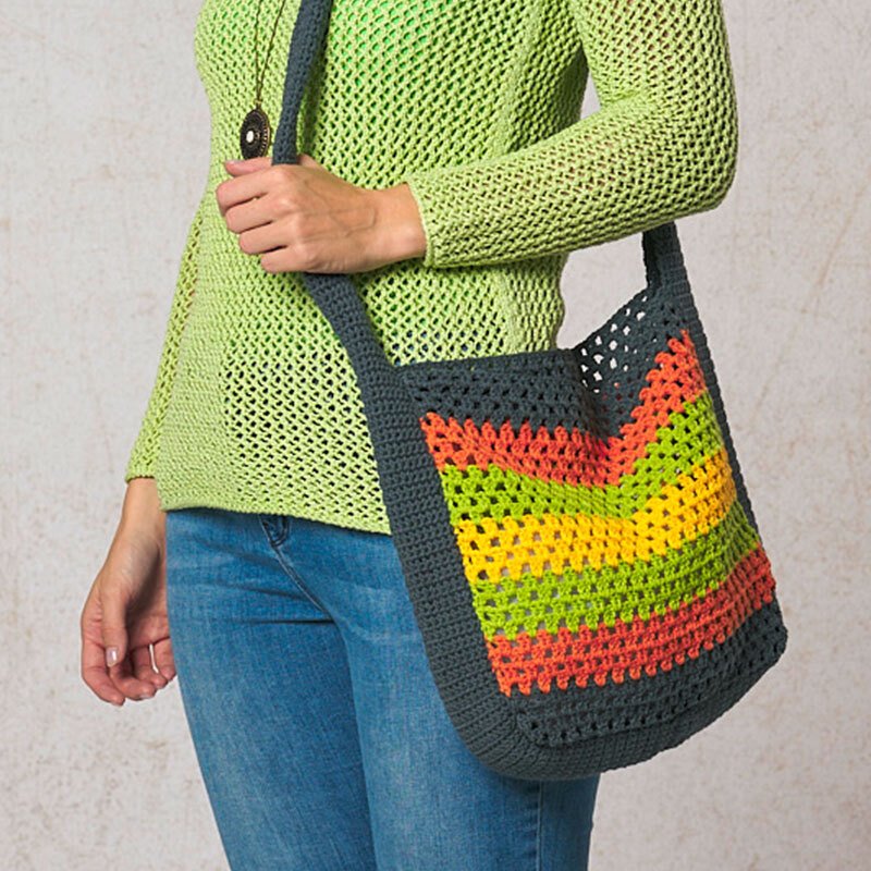 Gehäkelte Henkeltasche mit dunkelgrauem Rand und orangen, gelben und grünen Zickzackstreifen, an einer Schulter hängend.