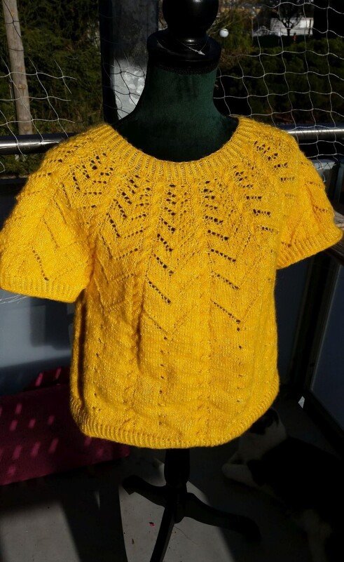 Gelbes, gestricktes Kurzarm-Shirt auf einer Schaufensterpuppe mit Ajour- und Zickzackmuster im oberen Bereich.