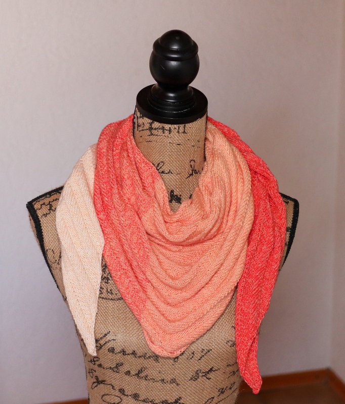 Triangle knitted shawl in cream to coral gradient draped on a dress form