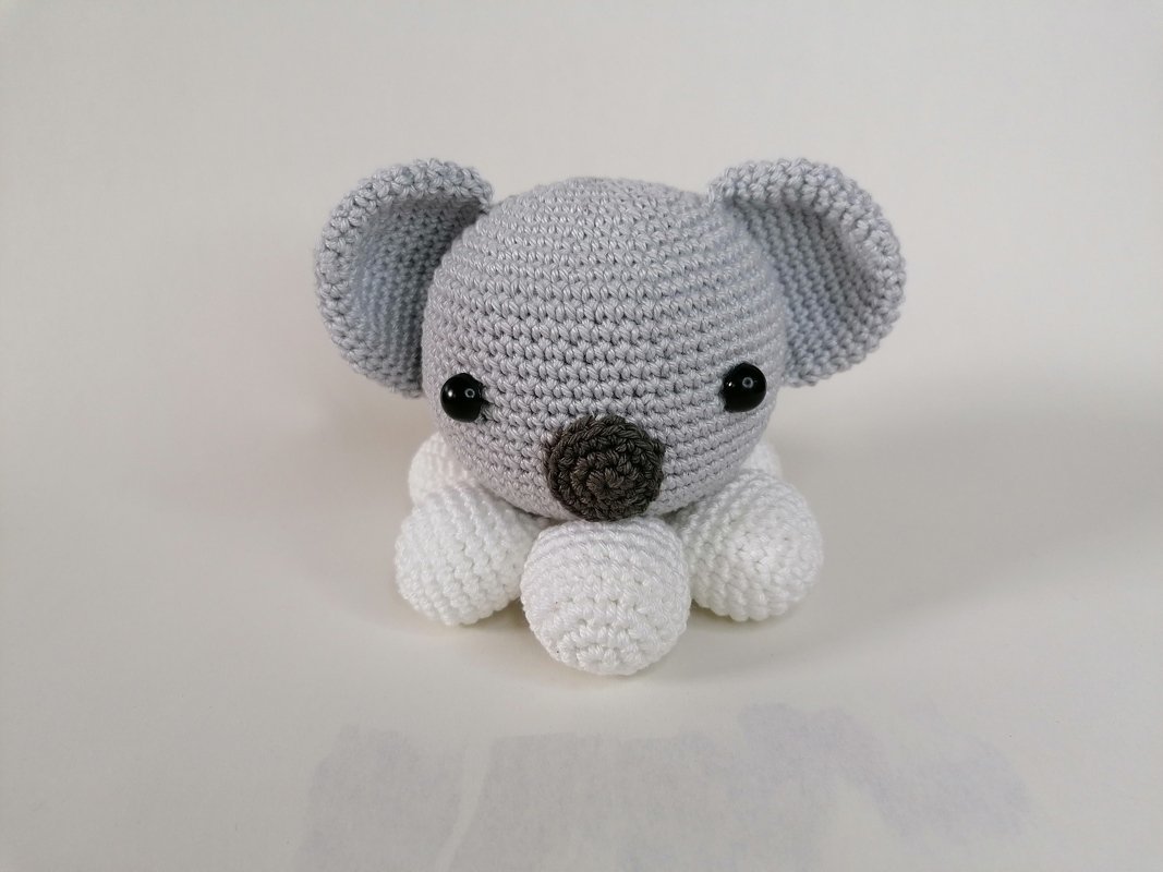 Gehäkelter Koala-Amigurumi, grau und weiß, mit schwarzen Augen auf hellem Hintergrund