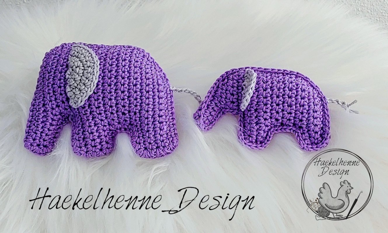 Zwei handgehäkelte lila Amigurumi-Elefanten mit grauen Ohren und Schwänzchen auf weißem, flauschigem Hintergrund