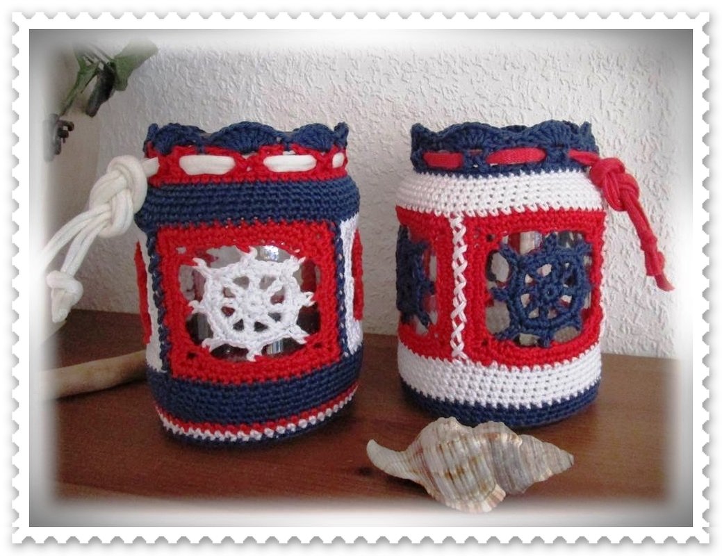 Zwei maritime gehäkelte Bezüge in Rot, Weiß und Blau um Kerzengläser mit Steuerradmotiven