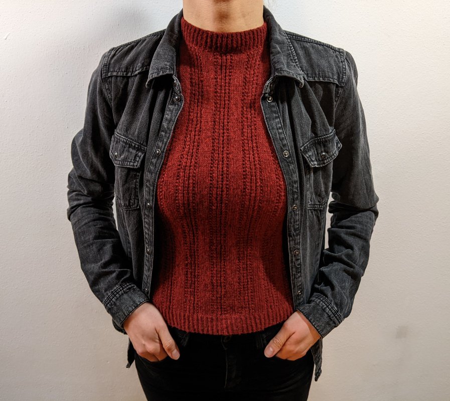 Oberkörper einer Person mit rostrotem, tailliertem Stricktop mit Stehkragen und dunkler Jeansjacke