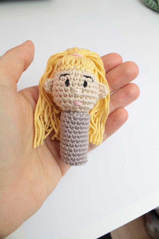 Gehäkelter Amigurumi-Puppenkopf mit blonden Garnhaaren in einer Hand gehalten