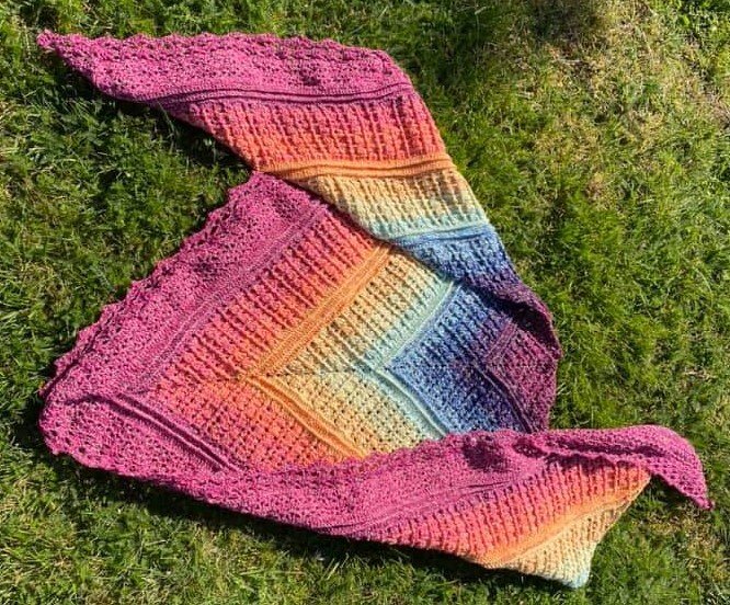 Gehäkeltes Dreieckstuch mit Regenbogen-Farbverlauf und Spitzenborte auf Gras