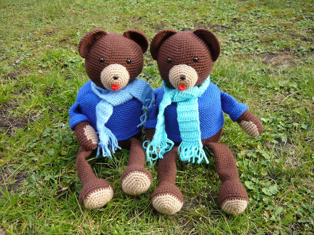 Zwei gehäkelte braune Teddybären mit blauen Pullovern und hellblauen Schals auf Gras