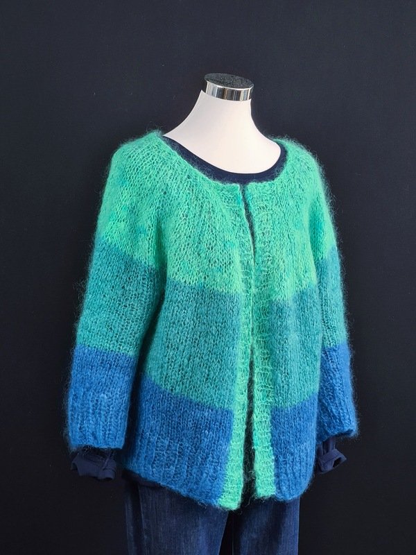 Flauschige, gestreifte Strickjacke in Blau-, Türkis- und Grüntönen an einem Mannequin