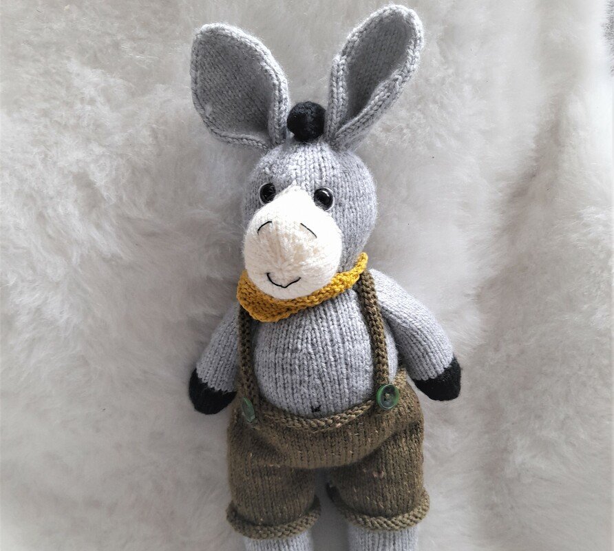 Gestrickter Amigurumi-Esel mit Trägerhose, gelbem Halstuch und schwarzen Pfoten