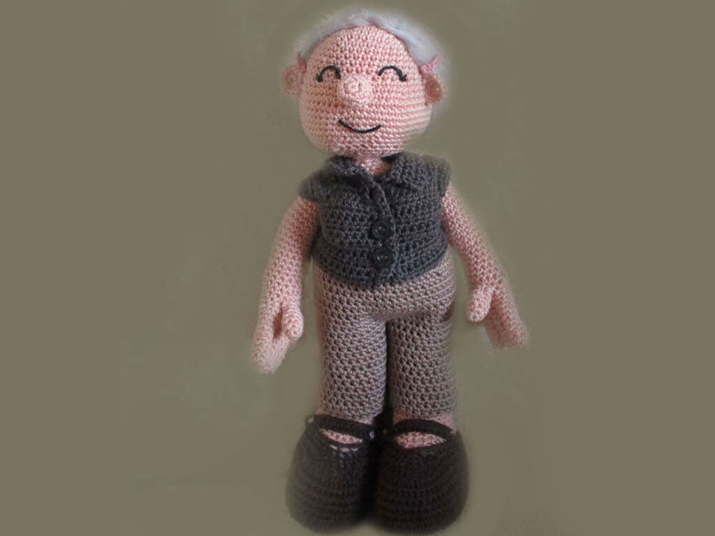 Amigurumi crochet doll of an elderly man with white hair, grey vest, grey pants, and brown shoes, smiling