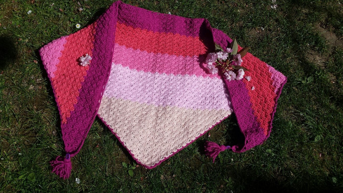 Gehäkeltes Dreieckstuch in Creme, Rosa und Magenta mit Quasten auf Gras liegend