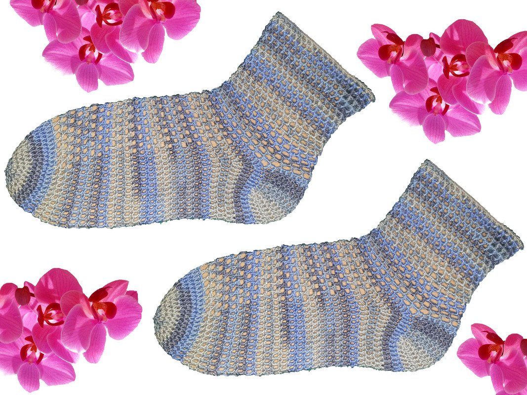 Gehäkelte Damensocken in Blau, Grau und Beige mit offenem Lochmuster, umgeben von pinken Orchideen auf weißem Hintergrund.