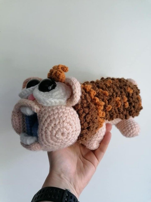 Hand hält gehäkeltes Amigurumi in Braun-, Orange- und Beigetönen mit großen schwarzen Augen und geöffnetem Mund