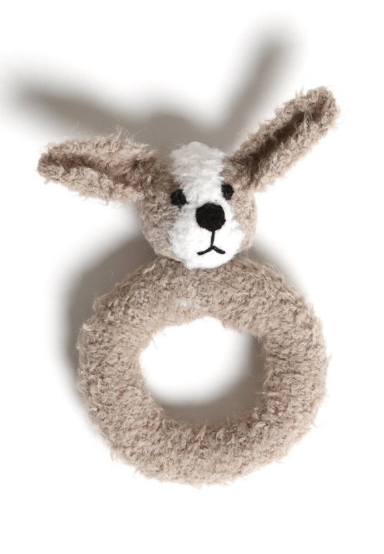Gestrickte Babyrassel in Hasenform mit beigem Greifring, beige-weißes Fell und aufgestickte schwarze Augen und Nase, auf weißem Hintergrund.