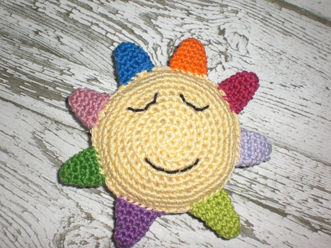 Gehäkelte gelbe Sonne mit bunten Zacken und gesticktem Lächeln