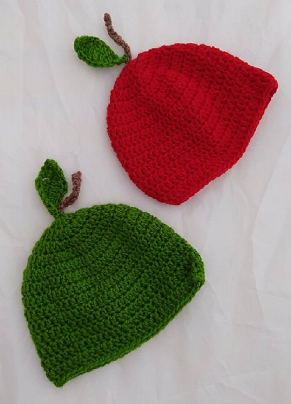 Rote und grüne gehäkelte Babymützen in Apfelform mit Blatt und Stiel