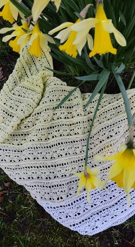 Gehäkeltes dreieckiges Tuch in hellem Gelb-Creme mit Lochmuster zwischen gelben Narzissen auf Gras