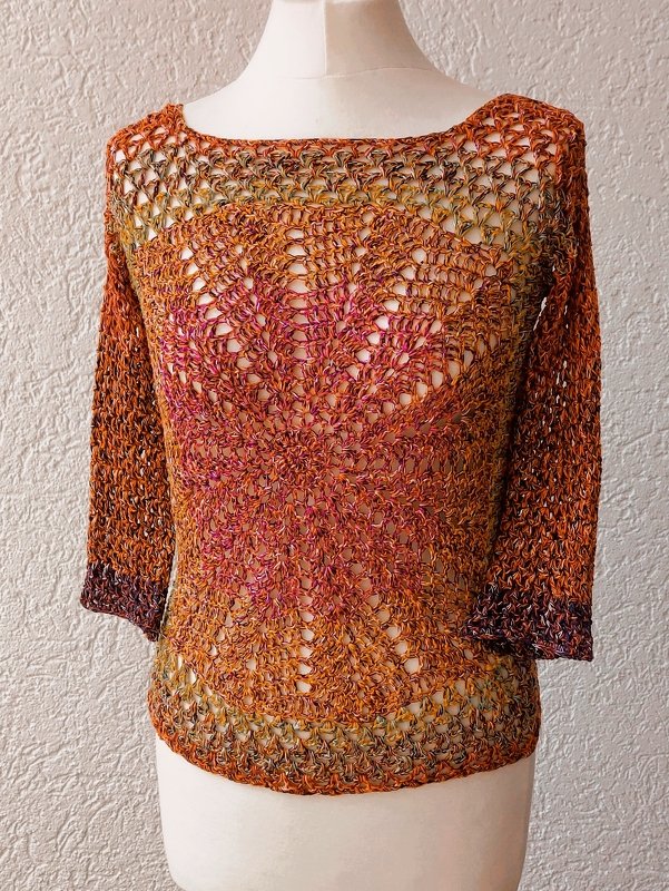 Gehäkeltes Damen‑Shirt in warmen Farben mit durchbrochenem Lochmuster, Boot‑Ausschnitt und Dreiviertelärmeln auf einer weißen Schneiderpuppe.