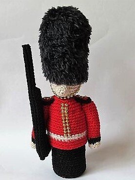 Gehäkelte Wachsoldatenpuppe in rotem Jackett, hoher schwarzer Bärenfellmütze und mit Spielzeuggewehr