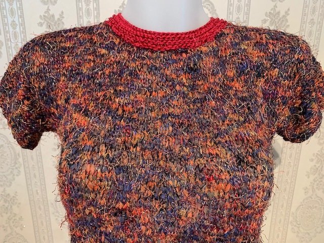 Mehrfarbiges Damen-Kurzarm-Strickshirt aus fransigem Garn in Orange, Blau und Violett mit rotem Rundhalsausschnitt auf Büste