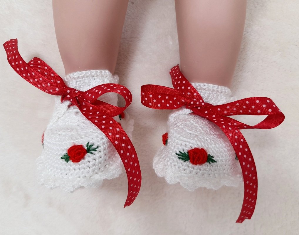 Weiße gehäkelte Babyschuhe mit rot gepunktetem Schleifenband und kleinem Rosenmotiv