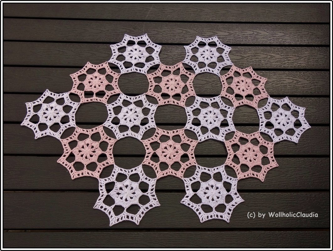 Rosa-weiße sternförmige gehäkelte Granny-Motive auf dunklem Holz