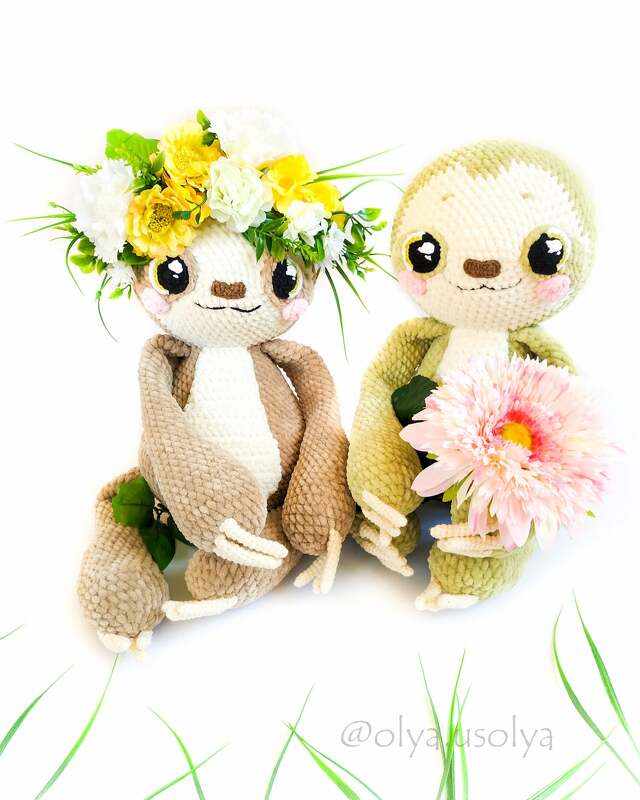 Zwei gehäkelte Faultiere, eines mit Blumenkranz, das andere mit rosa Blüte