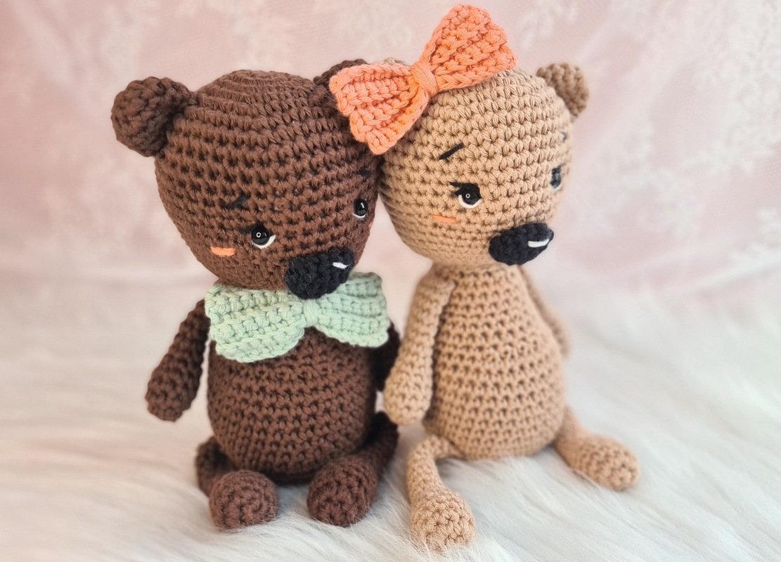 Zwei sitzende gehäkelte Amigurumi-Teddys, braun mit mintgrüner Fliege und beige mit korallfarbener Schleife