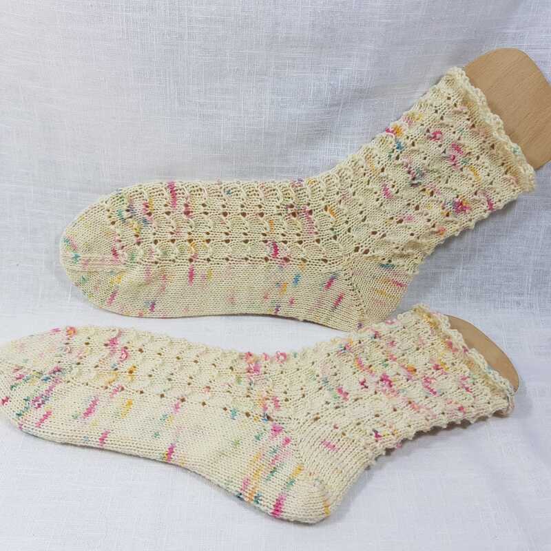 Gestricktes Sockenpaar in Creme mit Lochmuster und bunten Garnsprenkel auf hellem Stoff.