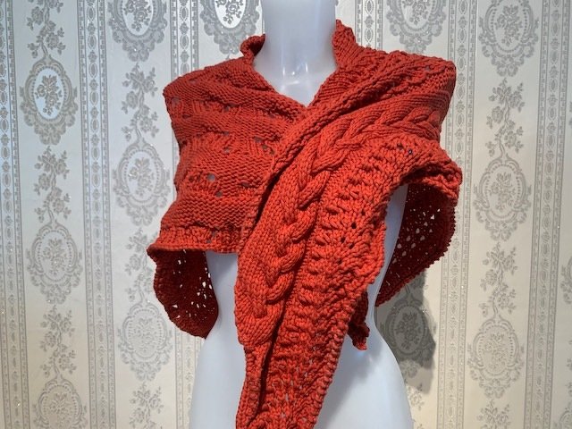 Orangerotes gestricktes Tuch mit Zopf- und Ajourmuster auf Schaufensterpuppe.