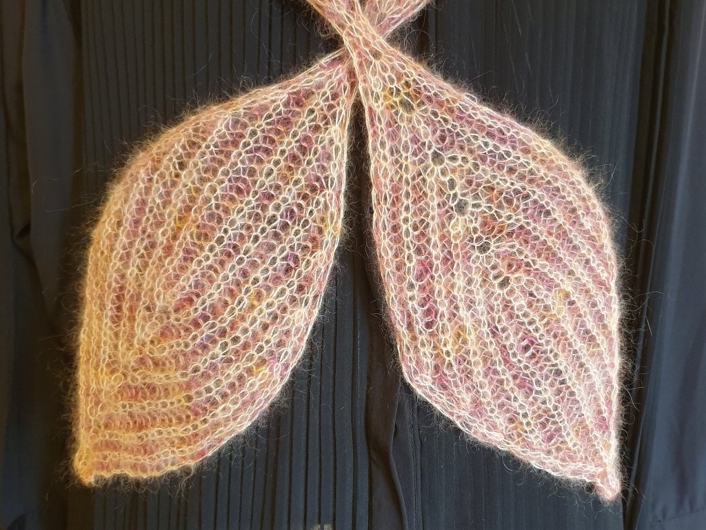 Zwei gestrickte, blattförmige Schalenden aus flauschigem, pastellfarbenem Garn vor dunklem Hintergrund