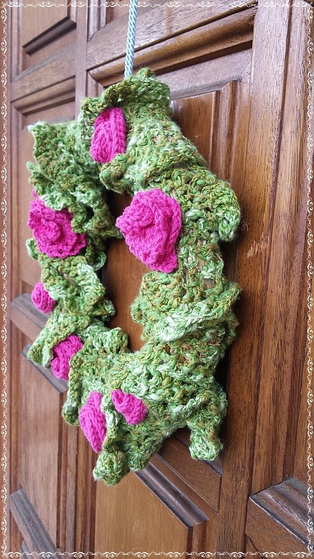 Gehäkelter grüner Türkranz mit pinken Rosen an Holztür