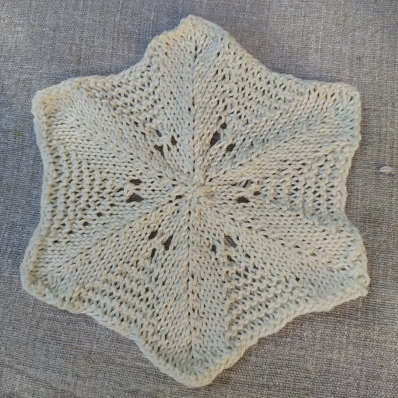 Cremeweiße gestrickte Stern-Applikation mit Lochmuster auf grauem Stoff