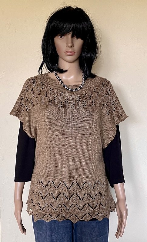 Schaufensterpuppe trägt sandfarbene gestrickte Tunika mit Ajourmuster am Ausschnitt und Zick‑Zack‑Saum über schwarzem Longsleeve.