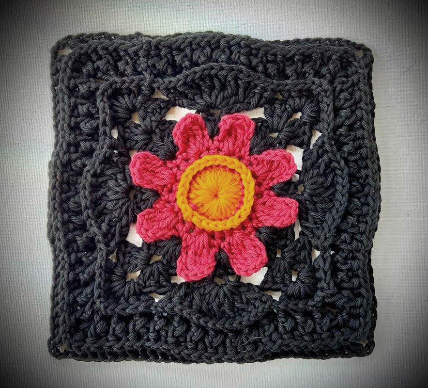 Gehäkeltes dunkles Quadrat mit rosa Blüte und gelbem Zentrum