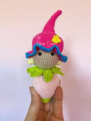 Gehäkelte Blütenelfe-Amigurumi mit spitzem pinken Hut, welliger blauer Borte und grünem Blattkragen