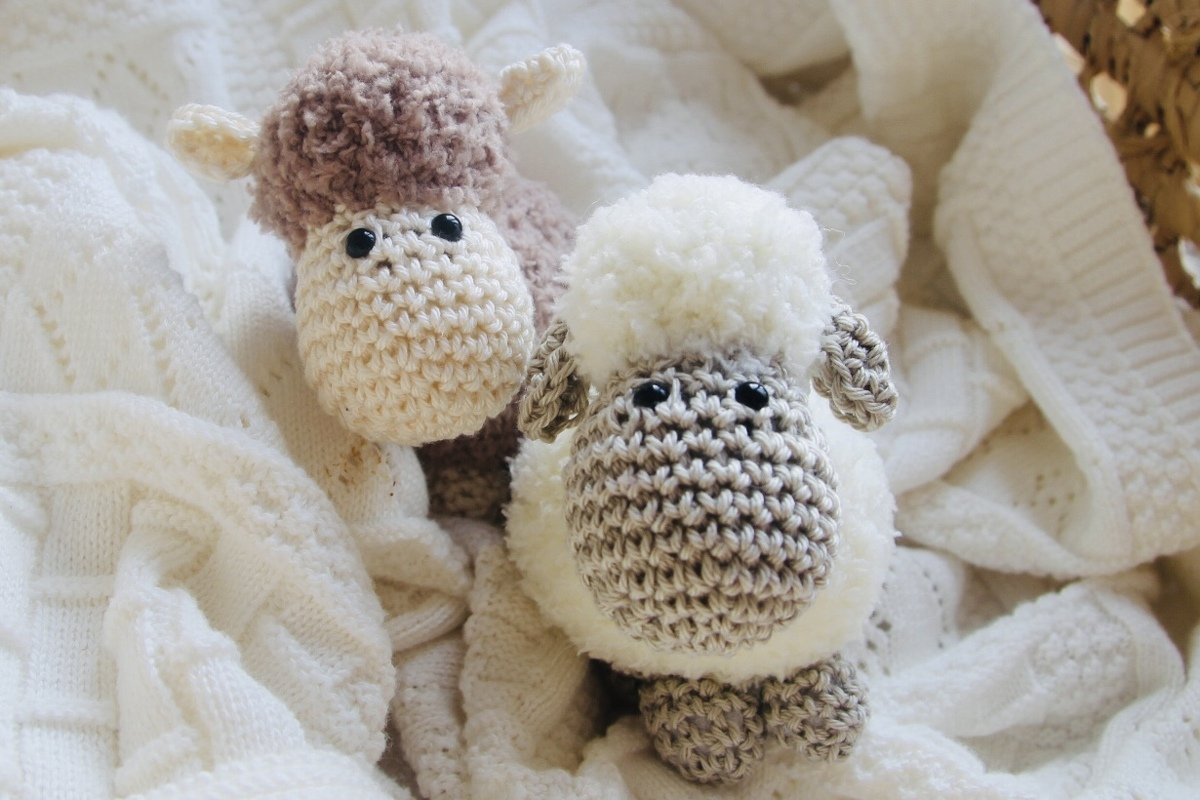 Zwei gehäkelte Amigurumi-Schafe (braun-beige und weiß-grau) auf einer strukturierten weißen Decke