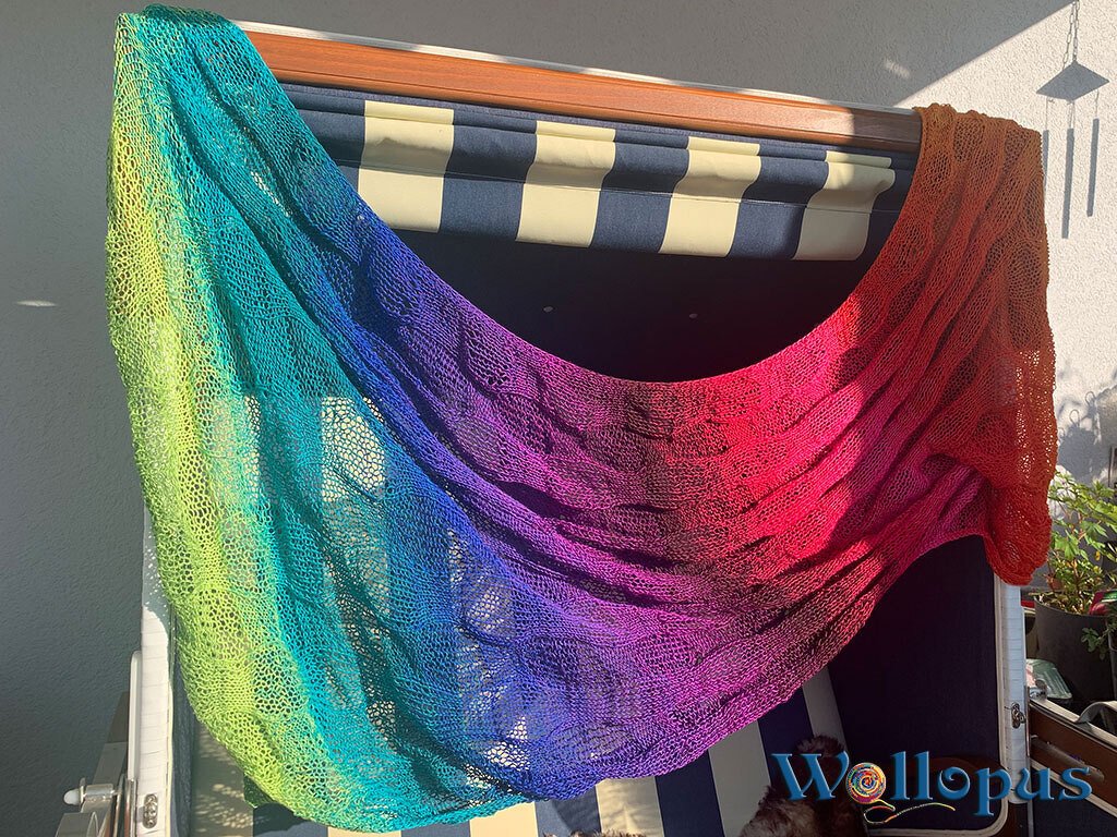 Gestricktes Verlaufstuch in Regenbogenfarben mit Lochmuster über einem Strandkorb drapiert